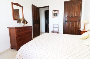 A bedroom with a bed, dresser, mirror, and a door leading to another room.