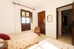 A bedroom with two beds, a chair, a wooden door, and a window with blinds.