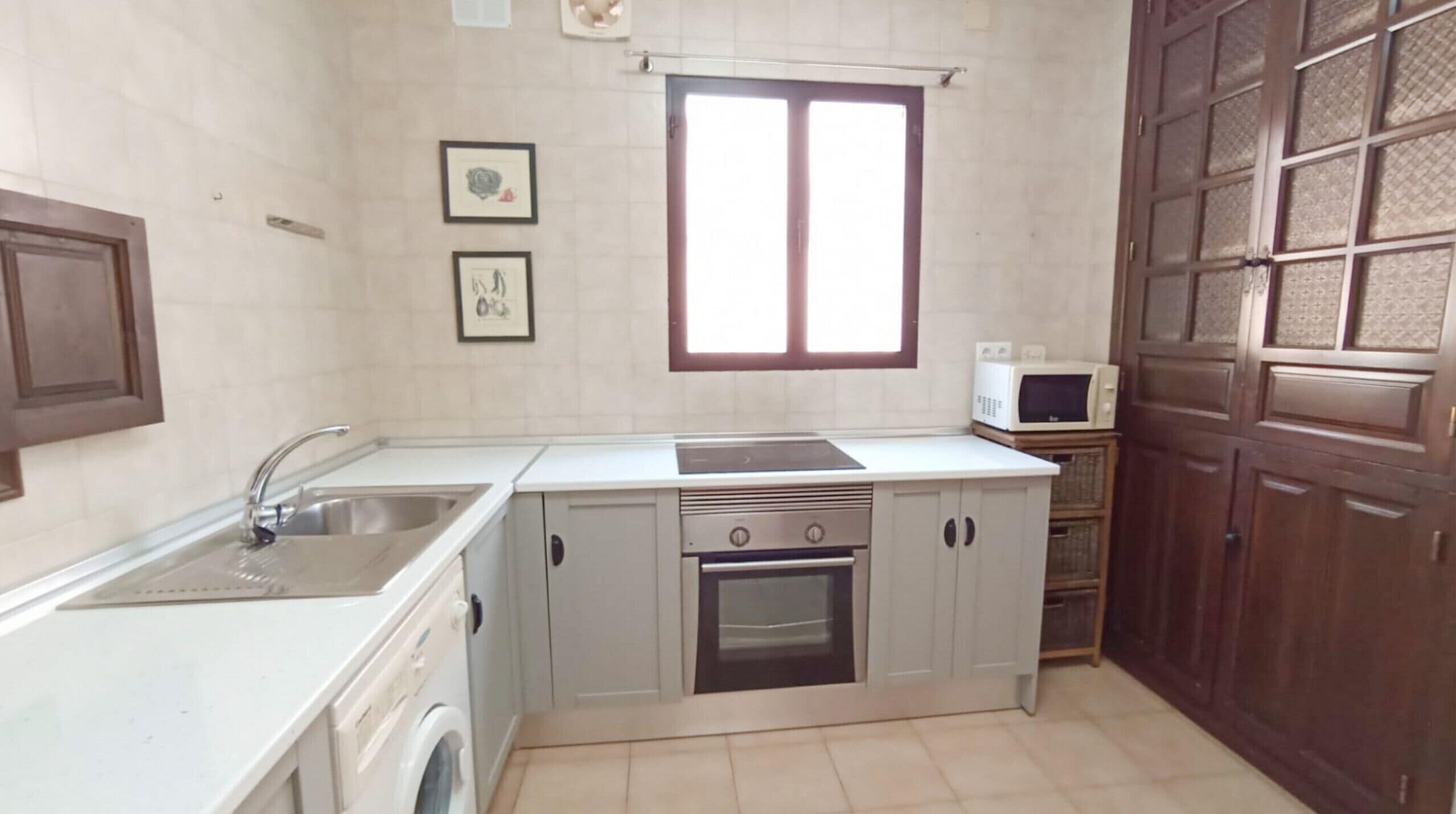 Una cucina compatta con lavello, piano cottura, forno e microonde. Alle pareti ci sono quadri incorniciati e una finestra sopra il lavello.