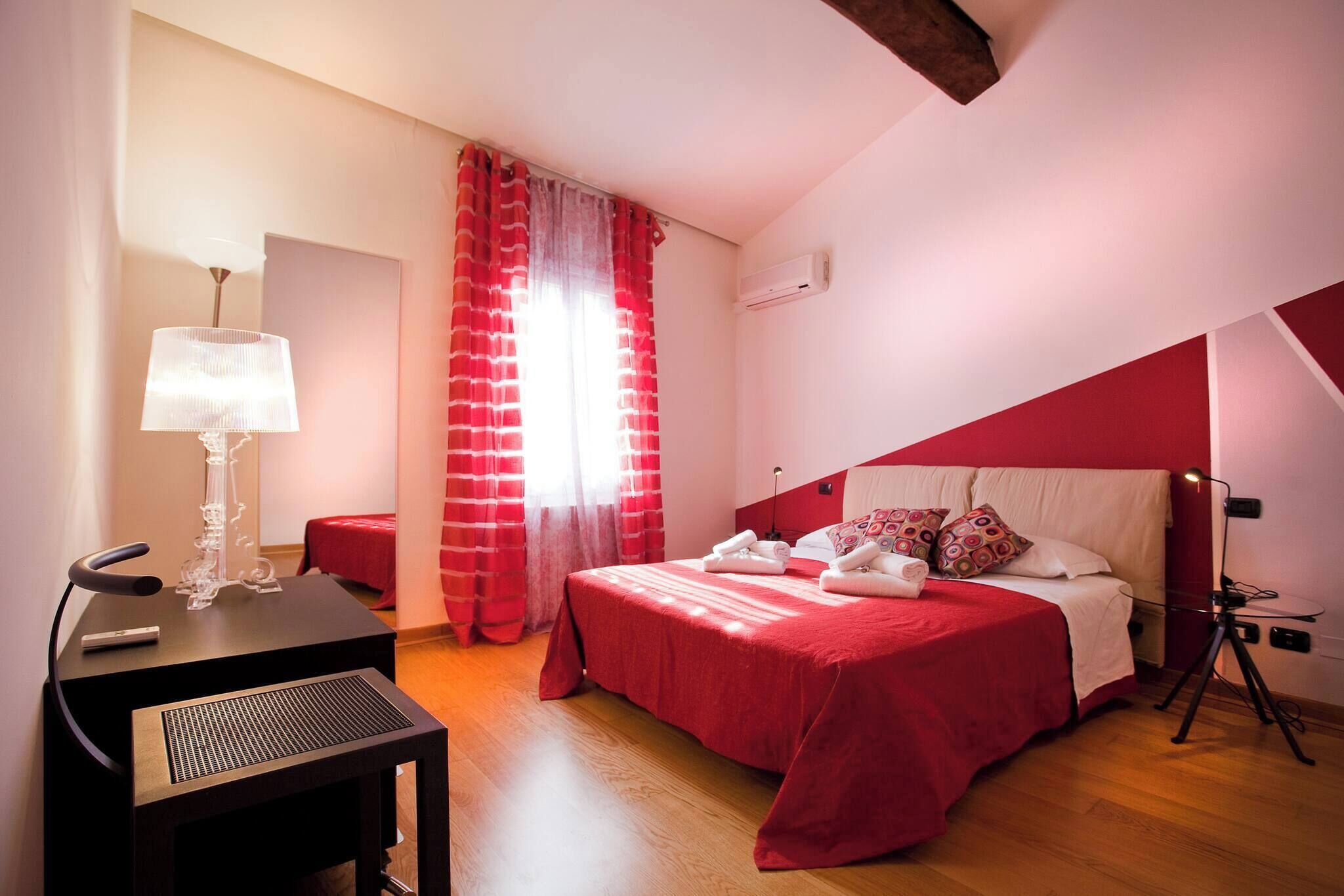 Una habitación de hotel con cama, escritorio, lámpara y ventana con cortinas.