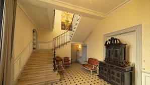 Un magnifique escalier avec un sol à carreaux, un lustre et une grande armoire en bois sombre.