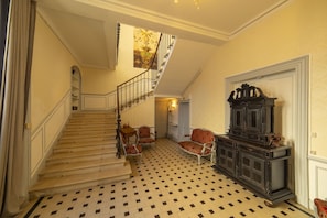 A grand staircase with a checkered floor, a chandelier, and a large dark wooden cabinet.