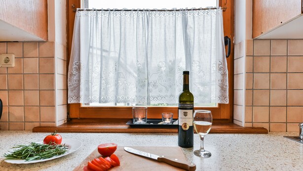 Una encimera de cocina con tabla de cortar, un cuchillo, un tomate, una botella de vino y una copa.