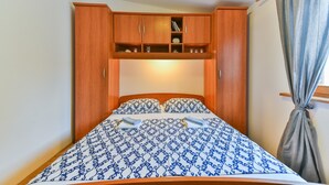 Un dormitorio con cama, armario de madera y una pequeña estantería.
