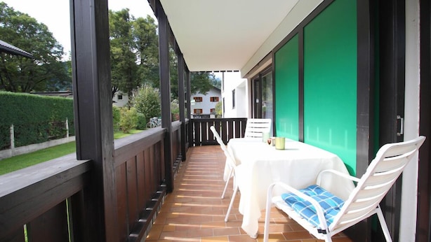 Eine überdachte Terrasse im Freien mit Tisch und Stühlen, einer grünen Wand und Blick auf eine Wohngegend.