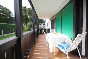 A covered outdoor patio with a table and chairs, a green wall, and a view of a residential area. - Anne (Garmisch-Partenkirchen)
