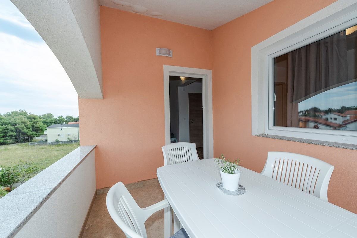 A balcony with a white table and chairs, a potted plant, and a view of the surrounding area.