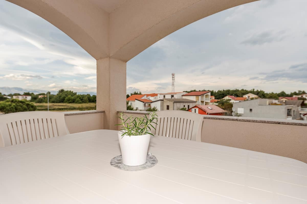 A balcony with a table and chairs, a potted plant, and a view of houses and a water tower in the background.