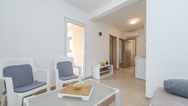A modern living room with white furniture, a glass coffee table, and a view into the kitchen. - Apartments Simic (Vir)