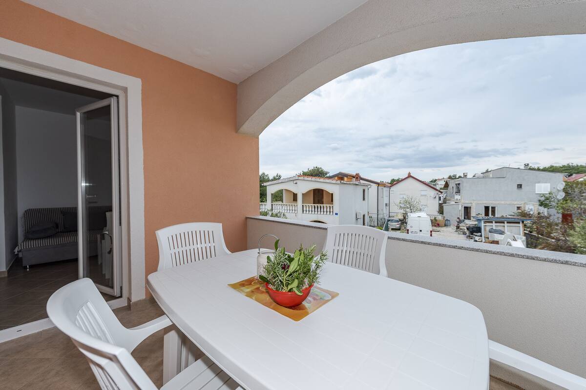 A balcony with a white table and chairs, a potted plant, and a view of neighboring houses.
