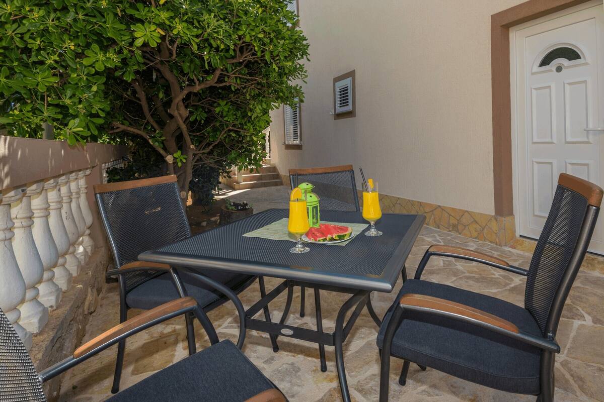 An outdoor patio with a table and chairs, a watermelon slice, and two glasses of orange juice.