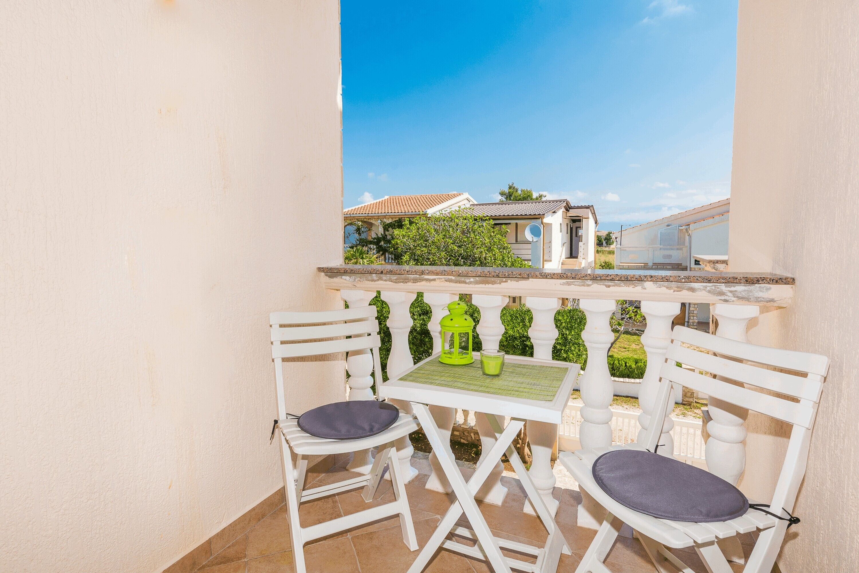 A balcony with two white chairs and a small table, a green lantern, and a clear view of the surrounding area.