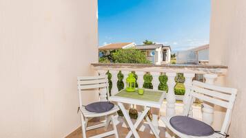 A balcony with two white chairs and a small table, a green lantern, and a clear view of the surrounding area.