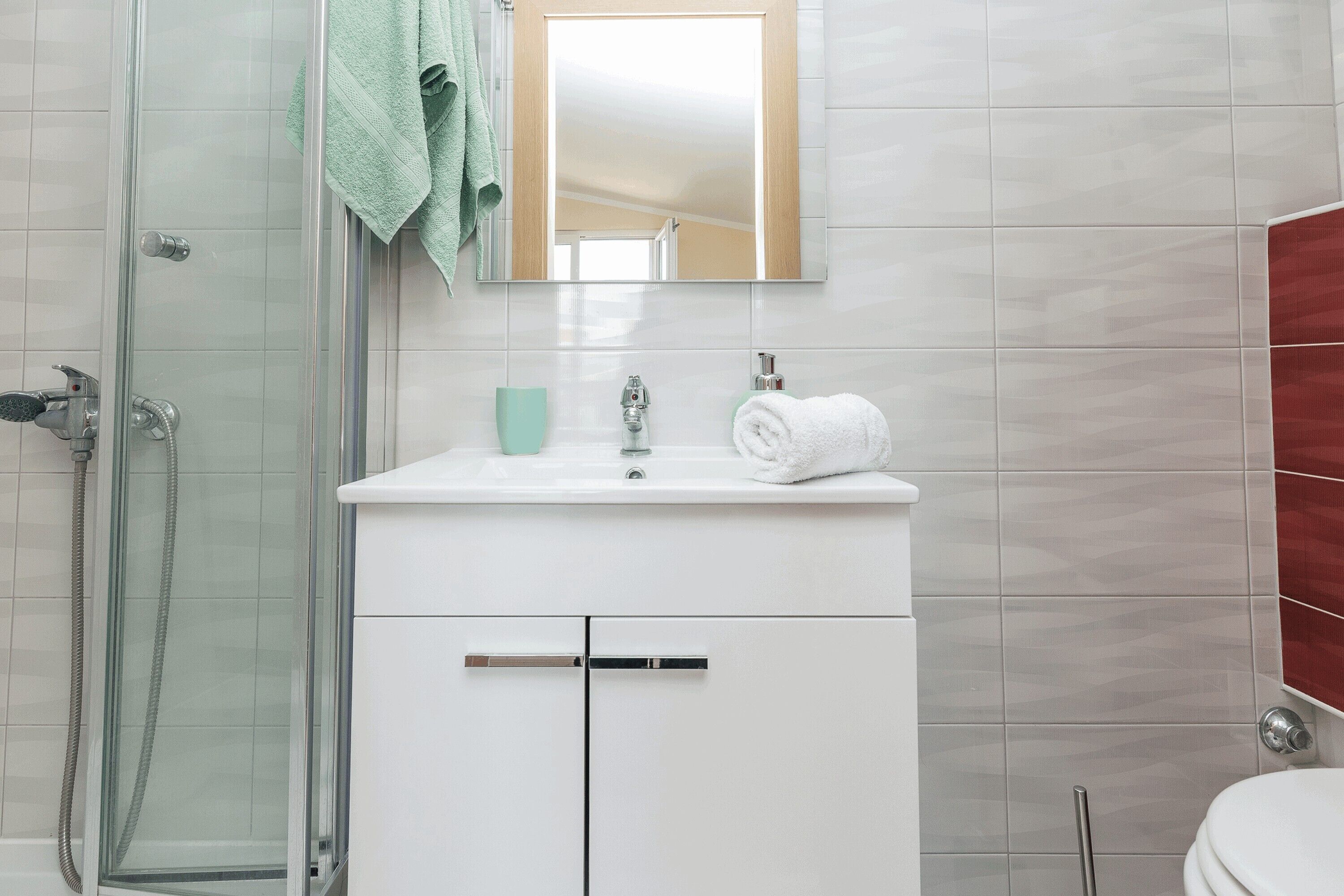 Ein Badezimmer mit Duschkabine aus Glas, einem weißen Waschbecken mit Spiegel darüber und einer Toilette.