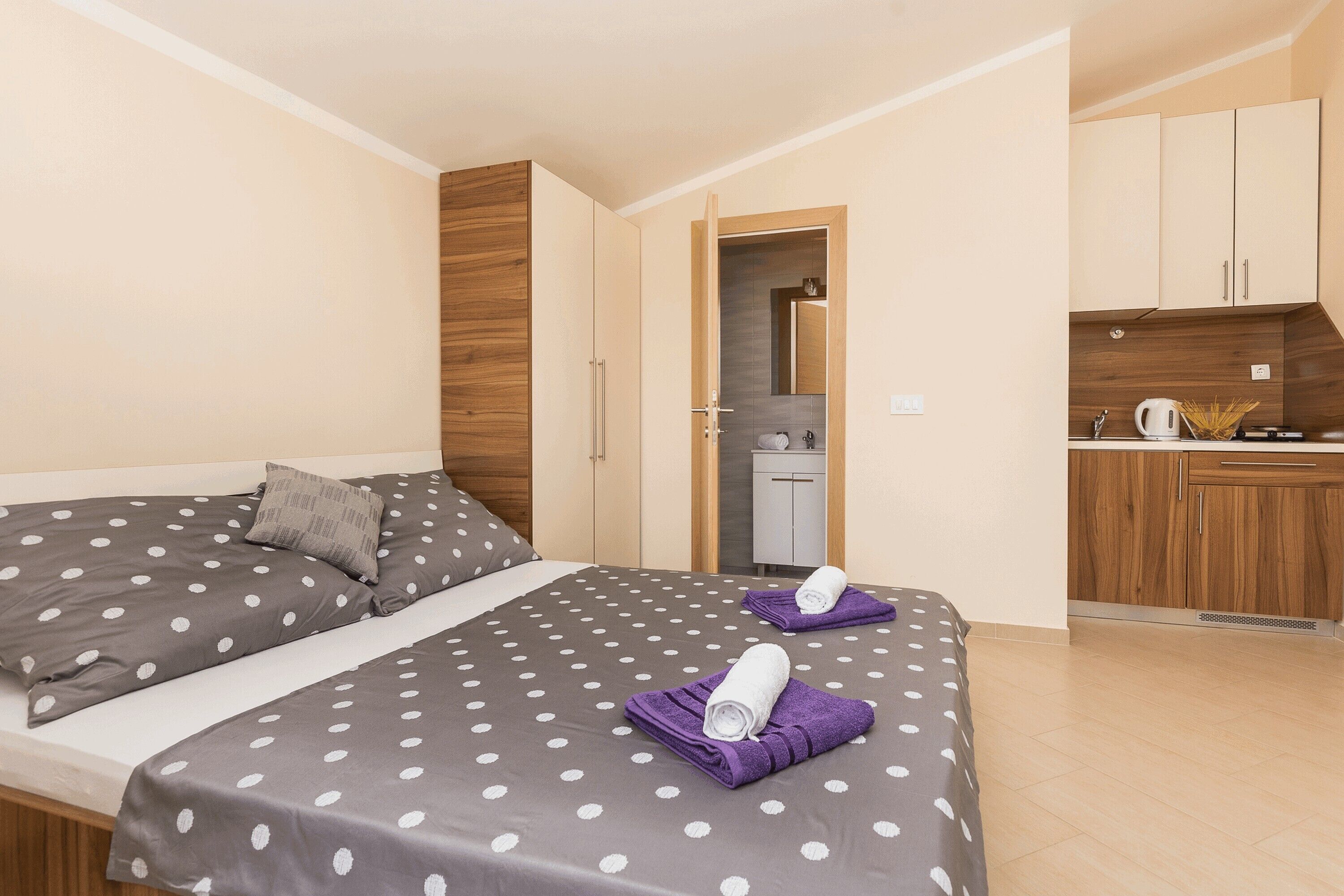 A bedroom with two beds, a small kitchenette, and a bathroom visible through an open door.