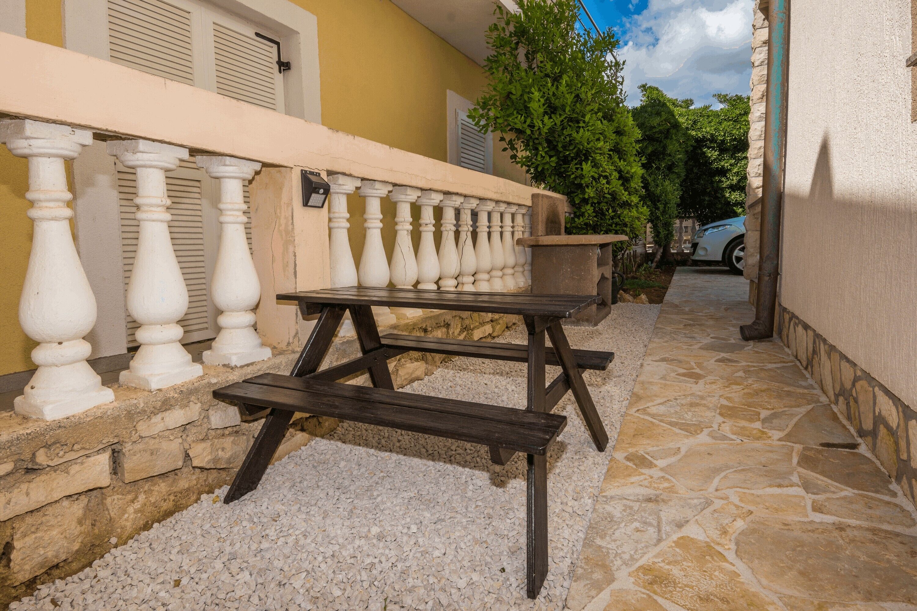 Un espacio al aire libre con pavimento de piedra, un banco de madera y una barandilla blanca.