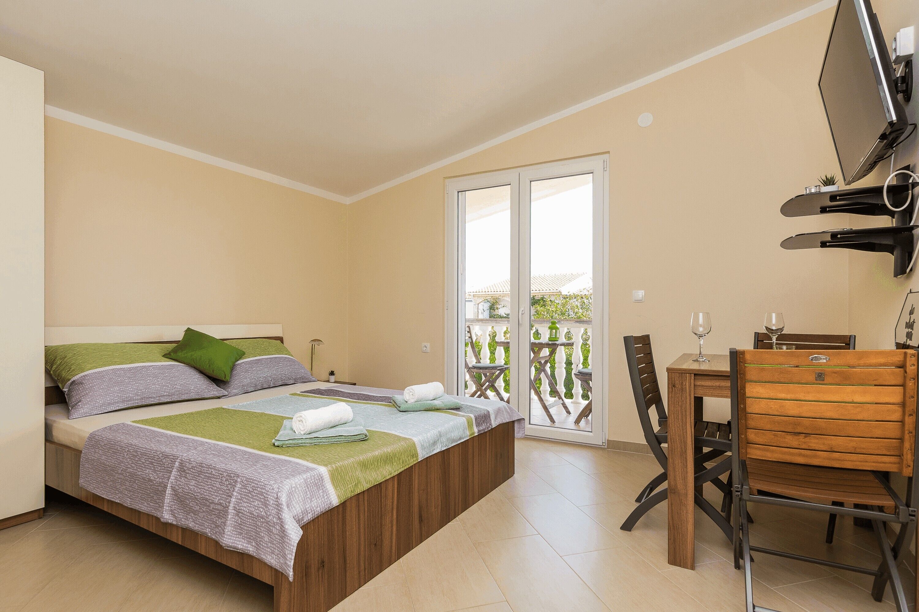 A bedroom with a bed, a desk, and a chair. There is a sliding glass door leading to a balcony.