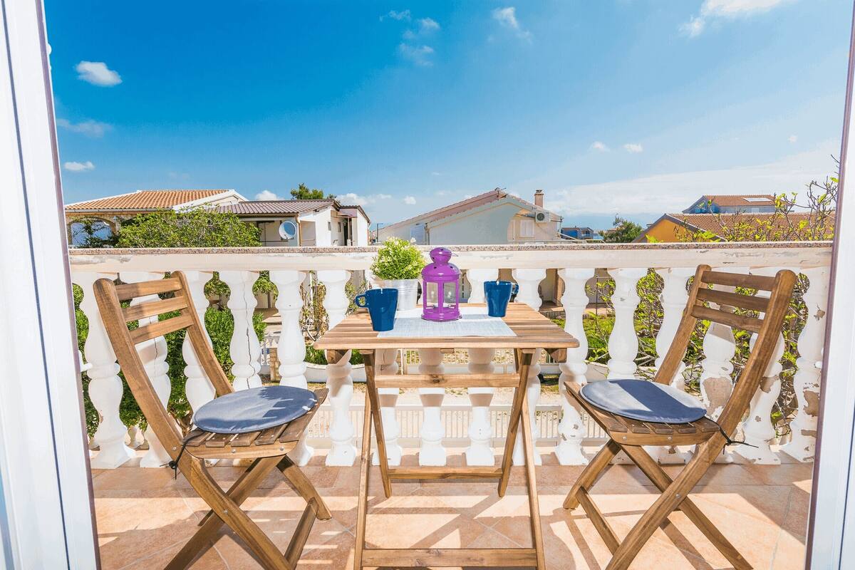 A wooden table with two chairs on a balcony with a white balustrade, a purple lantern, and blue cups.