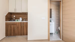 Eine moderne Küche mit Holzausstattung, einer weißen Arbeitsplatte und Blick in ein Badezimmer durch eine offene Tür.
