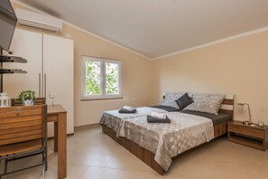 A bedroom with a bed, bedside table, lamp, and a window with a view of greenery. - Apartments Bobeta (Vir)