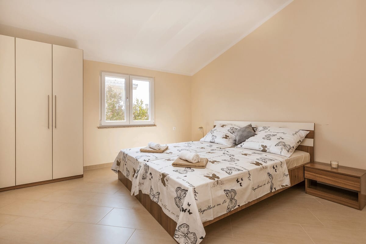 A bedroom with a bed, a nightstand, a wardrobe, and a window.