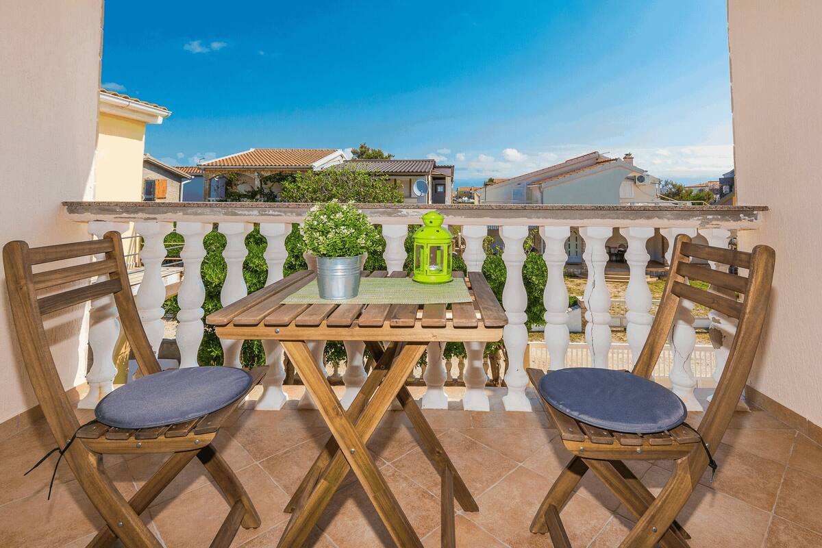 A wooden table with two chairs on a balcony, a potted plant, and a green lantern.