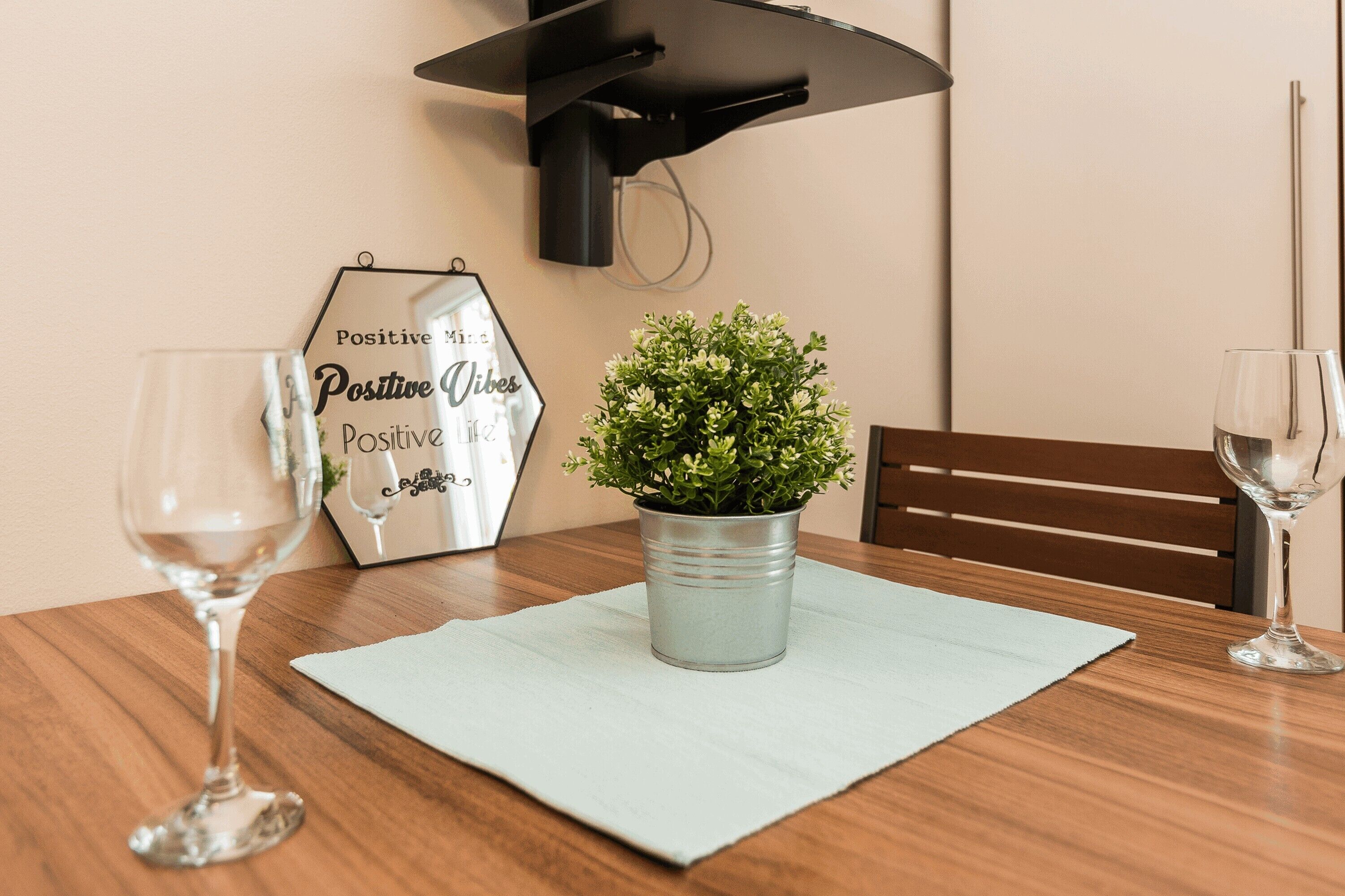 A dining table with a potted plant, two wine glasses, and a wall-mounted light fixture.