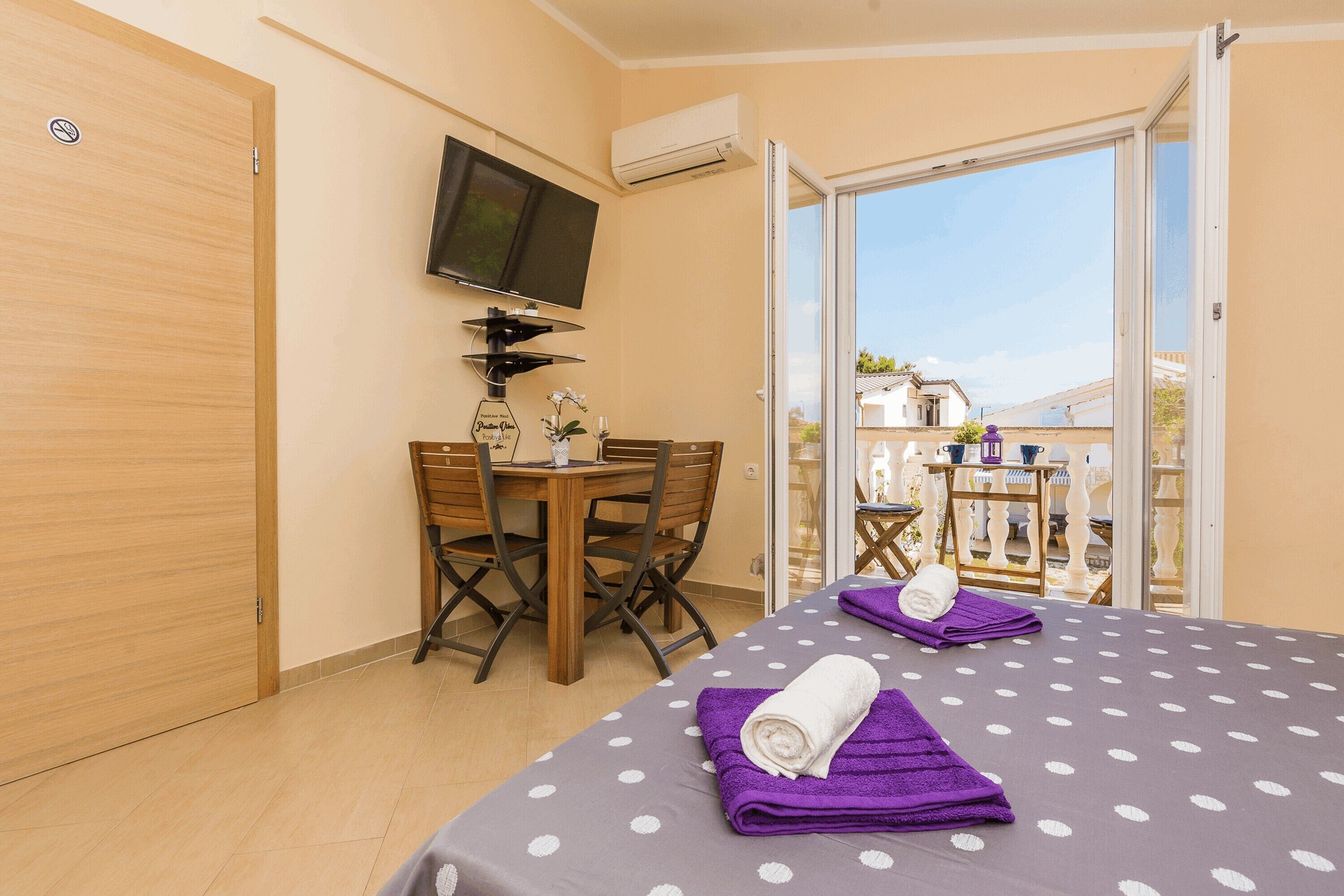A room with a bed, a table, chairs, a TV, and a balcony with a view.