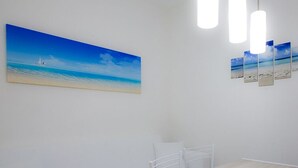 Casa de banho com uma grande pintura de uma praia, uma banheira branca e um candeeiro no teto.