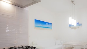Quarto moderno com parede revestida de azulejos brancos, uma pintura de uma praia, luminária pendente, mesa branca e uma TV sobre um móvel de madeira.