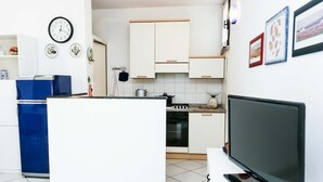 Une cuisine avec des meubles blancs, un réfrigérateur bleu, une horloge et un téléviseur.