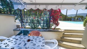 Un espace extérieur abrité avec une piscine, une table recouverte d’une nappe à motifs et un escalier menant à un niveau supérieur.
