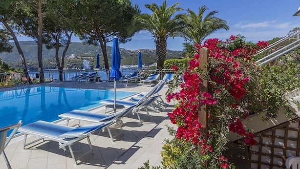 A swimming pool with lounge chairs and umbrellas, surrounded by trees and flowers. - Il Porto Bilocale 5 (Porto Azzurro)