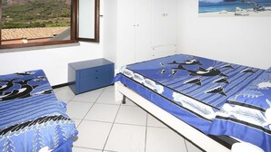A bedroom with two beds, a wardrobe, and a window with a view of a mountain and a beach. - Il Porto Bilocale 13 (Porto Azzurro)
