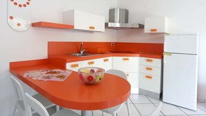 A compact kitchen with white cabinets, an orange countertop, a stainless steel range hood, and a white refrigerator. - Il Porto Bilocale 13 (Porto Azzurro)