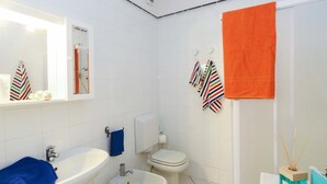 A bathroom with a sink, bidet, toilet, and a mirror. There are striped towels and an orange towel hanging on the wall. - Il Porto Trilocale 7 (Porto Azzurro)
