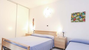 A bedroom with a wooden bed, a nightstand, a wall-mounted light, and a colorful artwork. - Il Porto Trilocale 7 (Porto Azzurro)