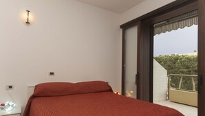 Un dormitorio con cama, mesita de noche, luz empotrada en la pared y puerta corrediza de vidrio que da a un balcón.