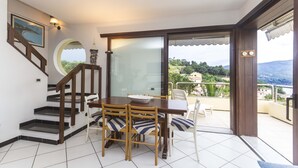 Un área de comedor con una mesa y sillas, una escalera y vistas a un balcón con barandilla.