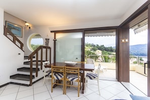 Uma área de refeições com mesa e cadeiras, uma escada e vista para uma varanda com guarda-corpo.