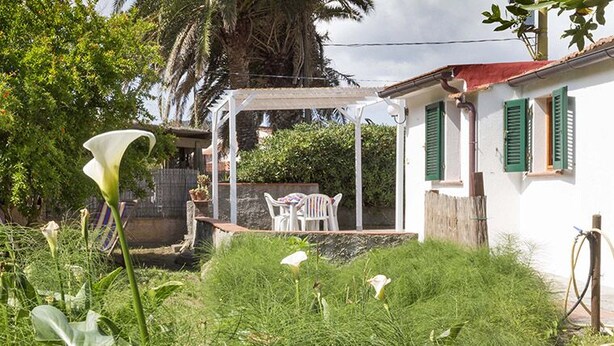 A garden with a white house, a pergola, and a table and chairs. - Appartamento Casa Plein Air  (Portoferraio)