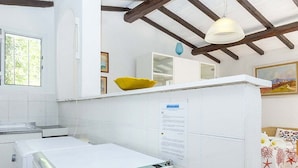 A kitchen with a sink, a white refrigerator, and a window. There is a white cabinet with a yellow pillow on top. - Appartamento Casa Plein Air  (Portoferraio)