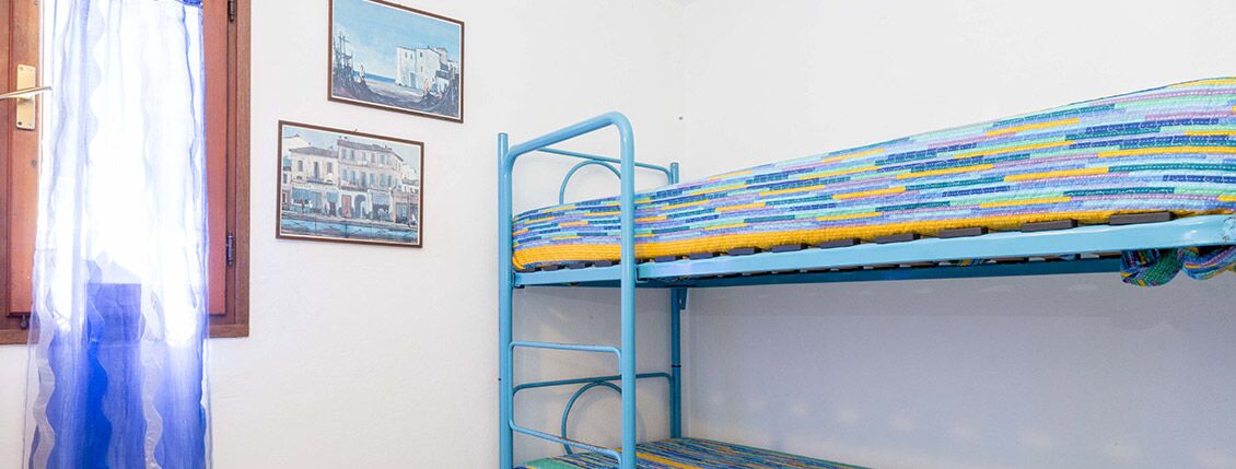 A bunk bed with a colorful striped mattress, a metal ladder, and two framed pictures on the wall.