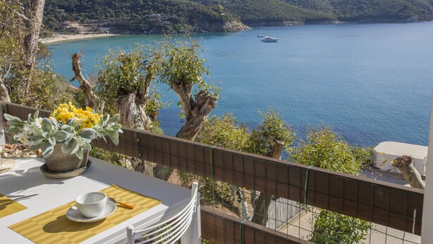 A terrace with a table set for dining, overlooking a coastal bay with boats and a mountainous backdrop. - Appartamento Casa Sabrina  (Portoferraio)