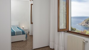A bedroom with a bed, a nightstand, a window with a view of the sea, and a radiator. - Appartamento Casa Sabrina  (Portoferraio)