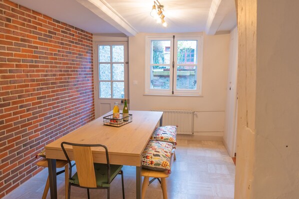 Ein Essbereich mit Backsteinwand, Holztisch, Bank und zwei Fenstern.
