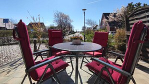 Eine Terrassengruppe im Freien mit einem runden Metalltisch und vier roten Sitzgelegenheiten mit Kissen.