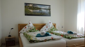 Een tweepersoonsbed met bloemenbeddengoed, twee kussens met vlinderprint, een bedlampje en een lijst met een foto van een meer aan de muur.