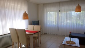Ein Zimmer mit Esstisch, Stühlen, Fernseher, Sofa und einem kleinen Tisch mit einer Vase.