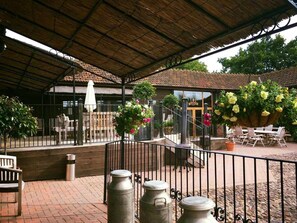 An outdoor patio area with a covered roof, seating arrangements, and potted plants. - Muddifords Court (Tiverton)